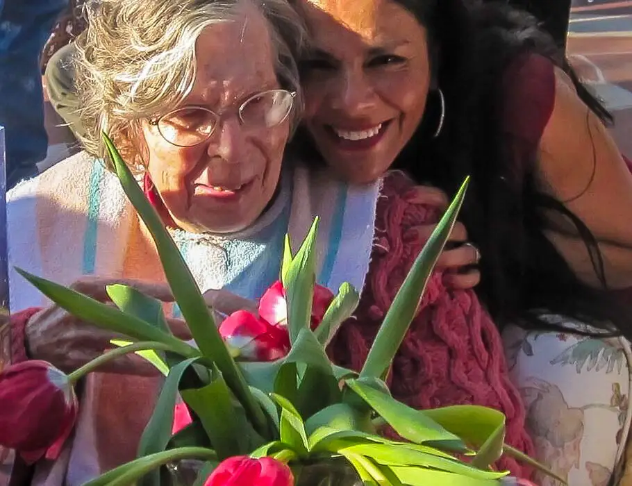 A senior and a caregiver holding a plant smiling on the camera.