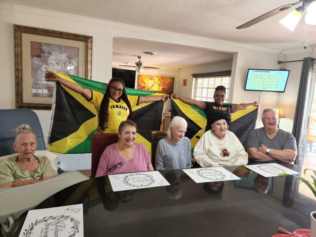 A group of seniors sitting at a table and two woman at their back holding a flag.